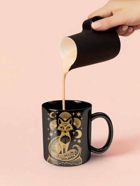A black ceramic mug featuring a stylized golden fox design surrounded by Art Deco ginkgo fans, crescent moons, and stars. The mug has a glossy finish and ergonomic handle.